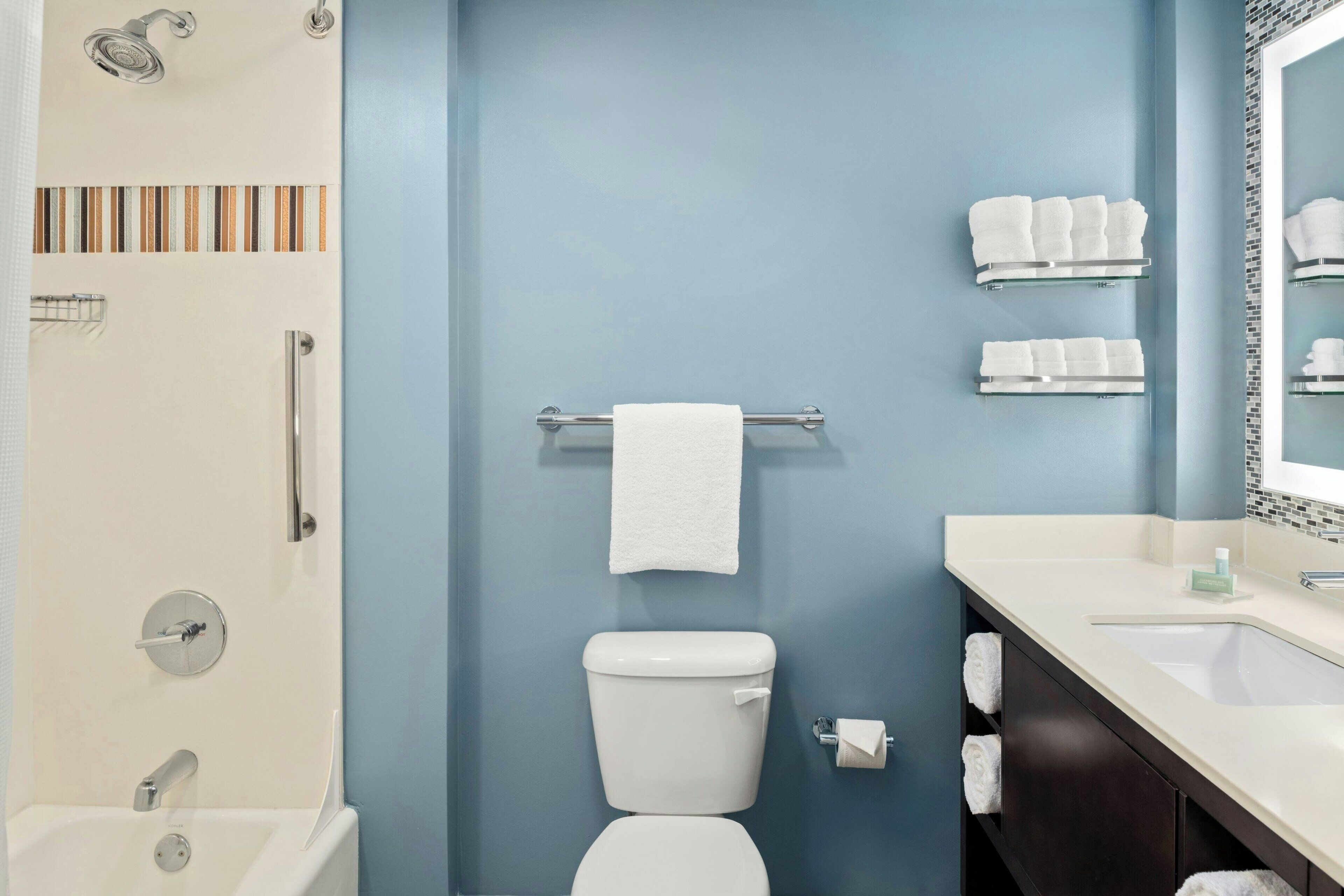 Un baño con pared azul, inodoro blanco, cabina de ducha de vidrio y tocador con espejo.