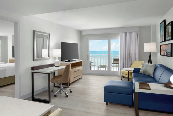 Habitación de hotel con cama, escritorio, silla, sofá y balcón con vista al mar.