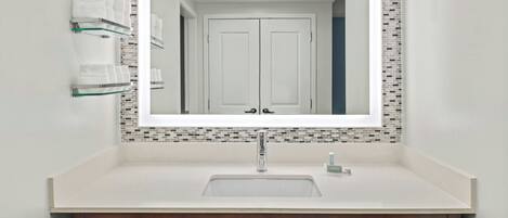 A bathroom with a white sink, a mirror with a mosaic tile border, and two towel dispensers.