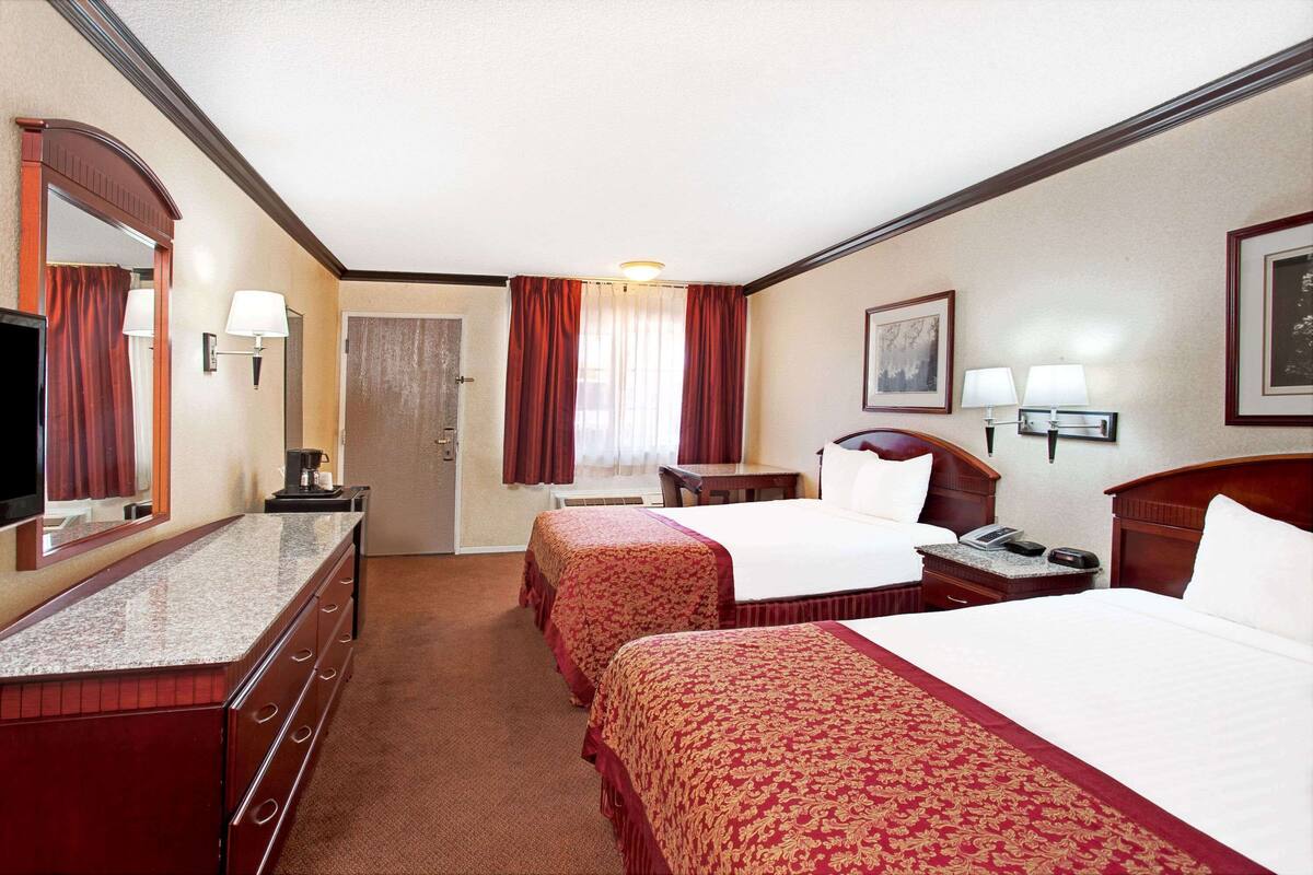 A hotel room with two beds, a desk, a chair, a television, and a door.