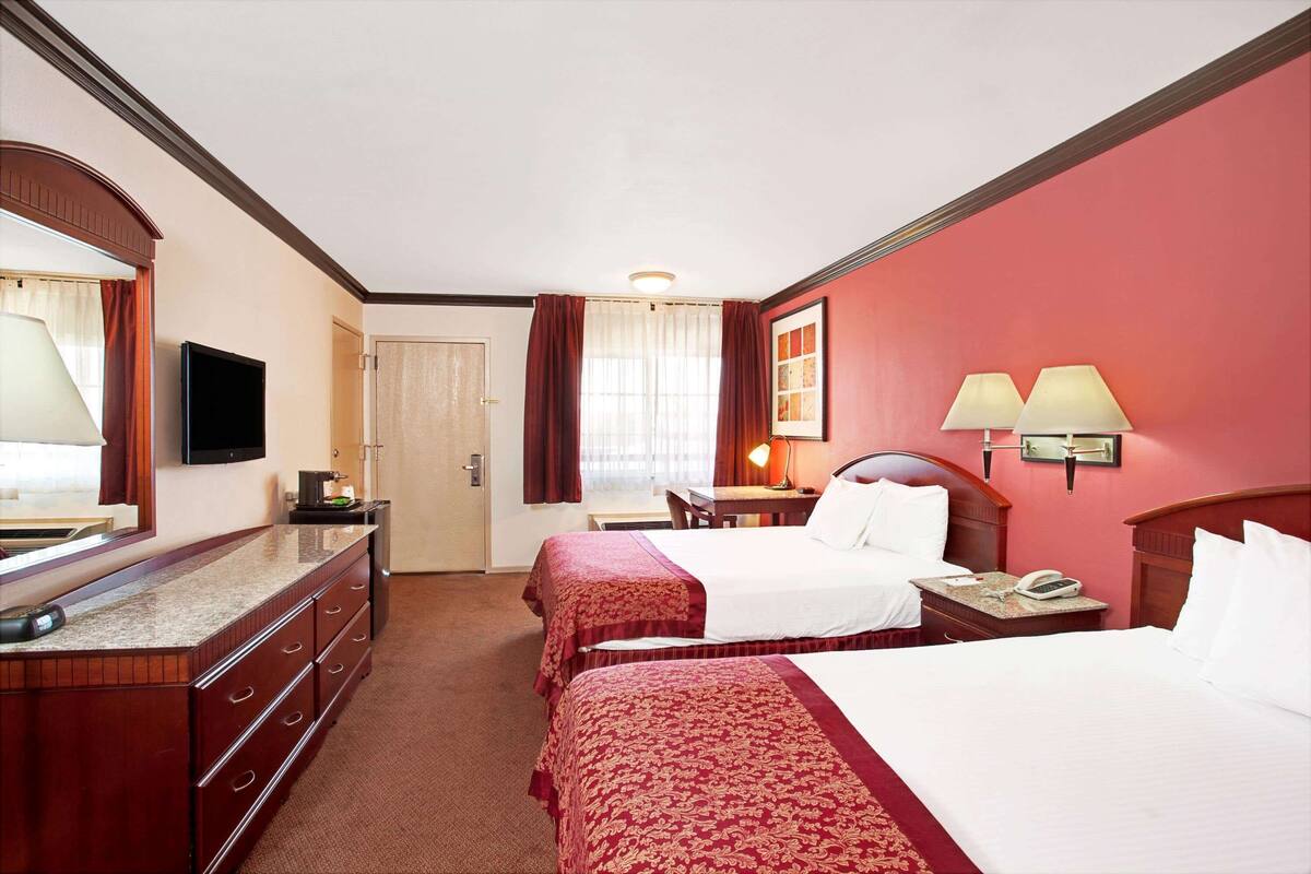 A hotel room with two beds, a desk, a TV, and a bathroom.