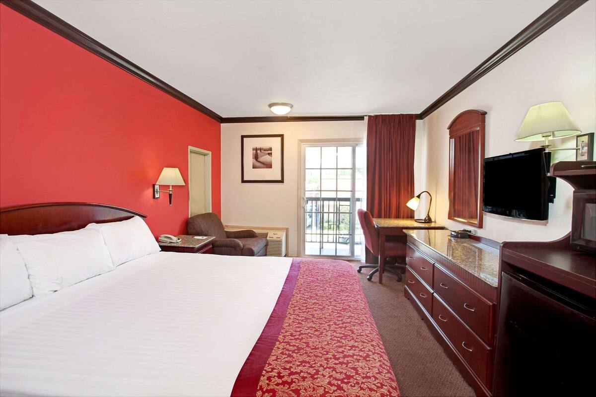 A hotel room with a large bed, a desk with a lamp, a television, and a window with curtains.