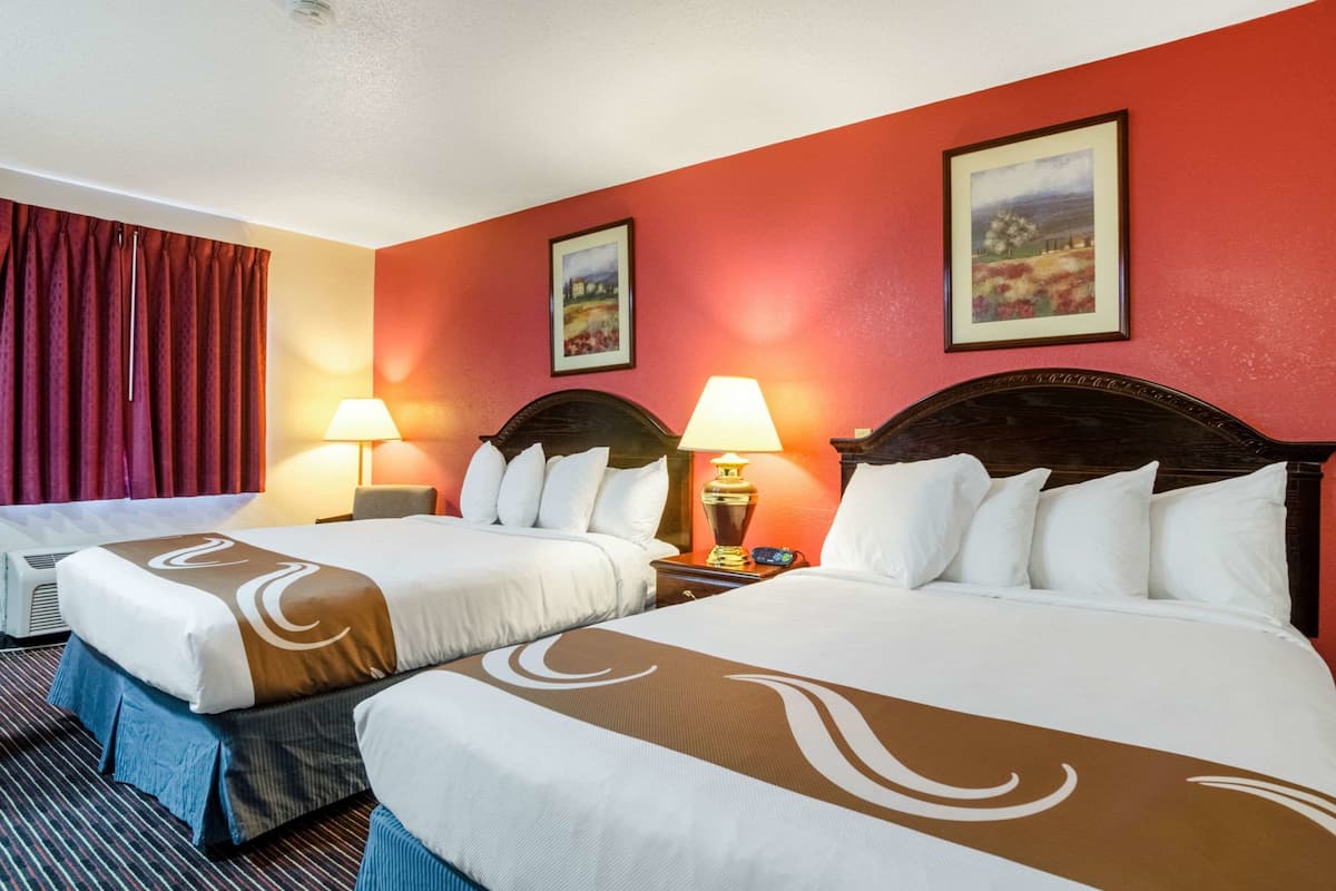 A hotel room with two beds, red walls, and two paintings.