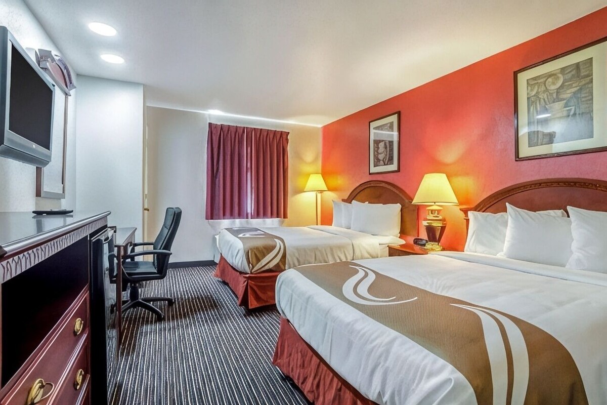 Une chambre d’hôtel avec deux lits, un bureau, une chaise et un téléviseur.