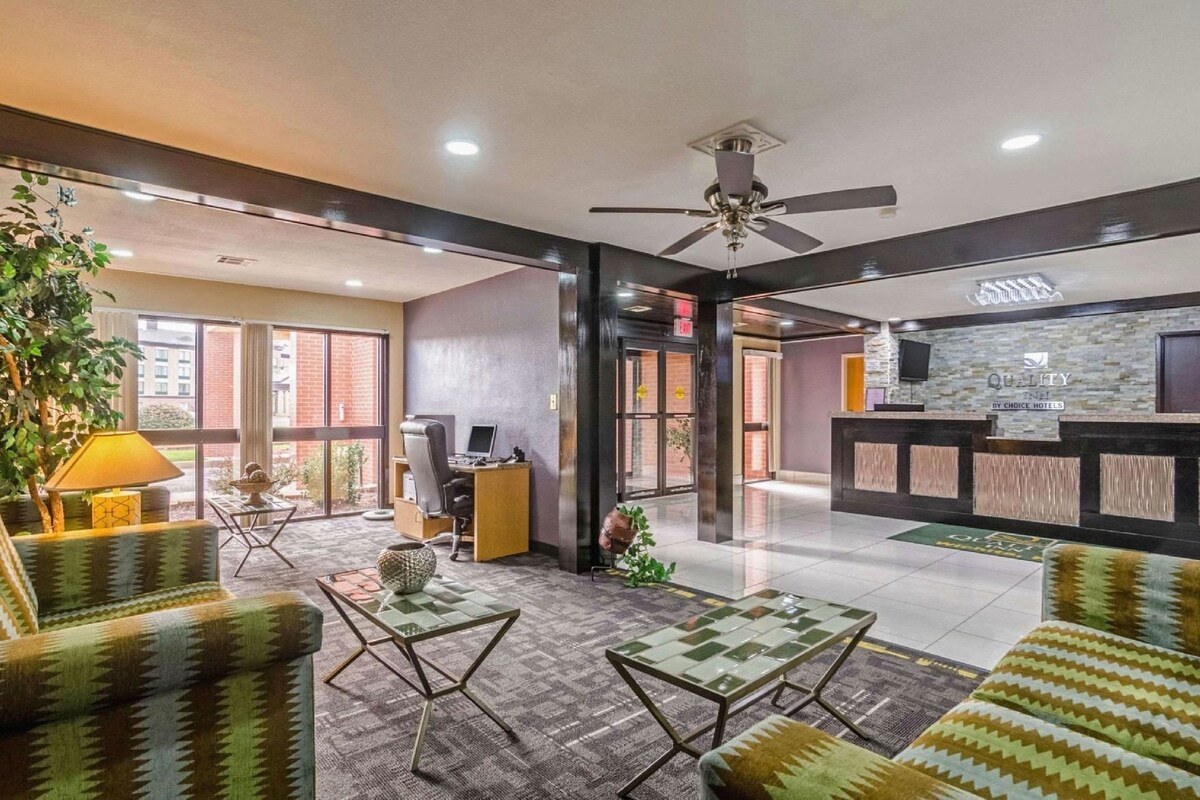 Un hall d’hôtel comprenant un comptoir d’accueil, un espace salon avec des canapés et des tables aux motifs décoratifs, un bureau avec un ordinateur et un ventilateur de plafond.