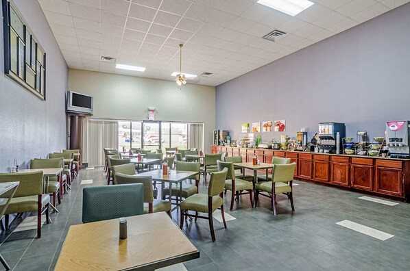 A restaurant with multiple tables and chairs, a counter with a menu, and a television mounted on the wall.