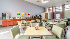 A spacious dining area with multiple tables and chairs, a kitchen counter with various food items and equipment, and a large window providing natural light.