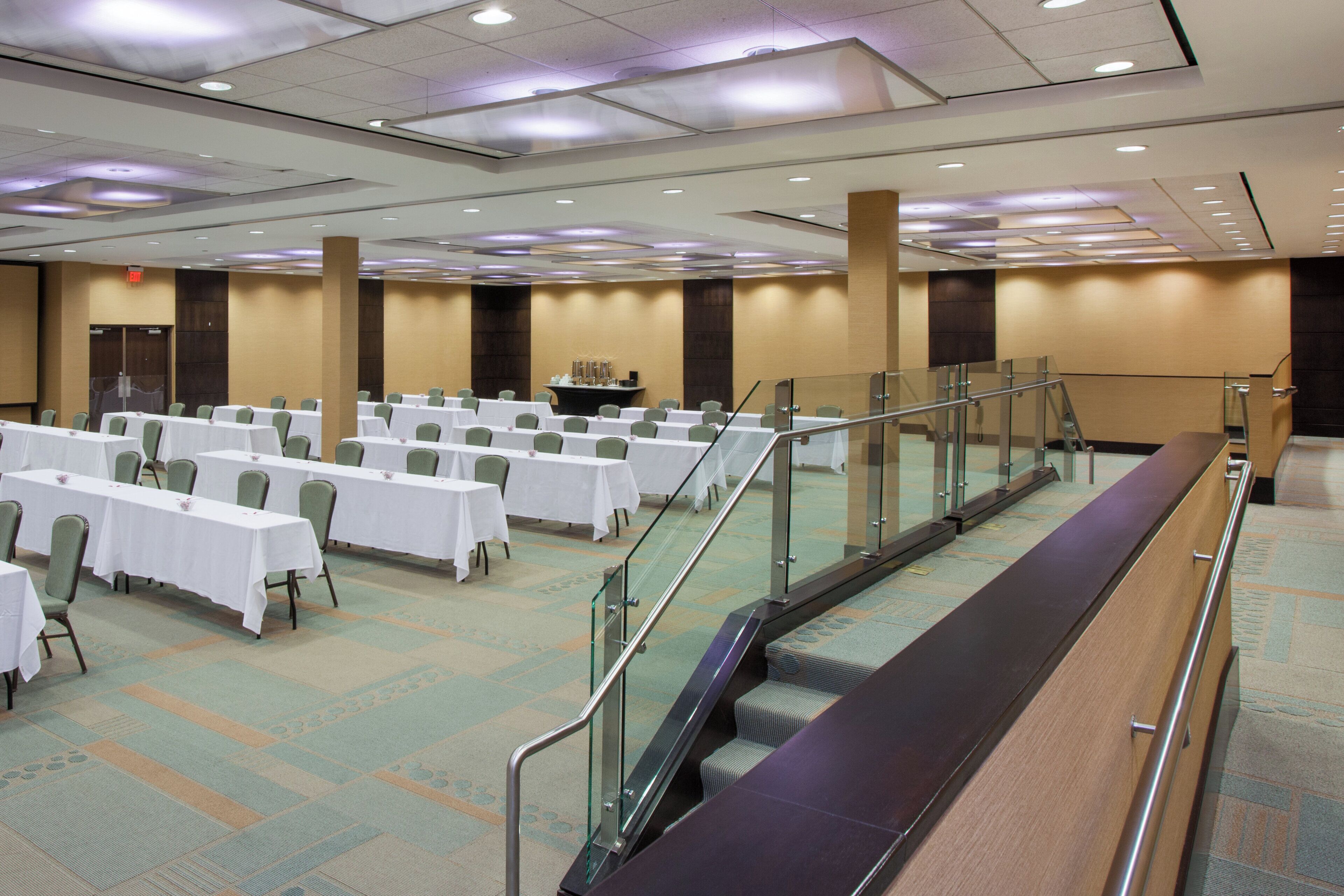 A conference room with rows of tables and chairs, a stage with a podium, and an escalator.