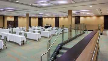 A conference room with rows of tables and chairs, a stage with a podium, and an escalator.