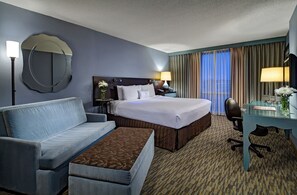 A hotel room with a bed, a sofa, a desk, a chair, a lamp, a mirror, and a window with curtains. - Crowne Plaza Lombard Downers Grove by IHG (Glen Ellyn)