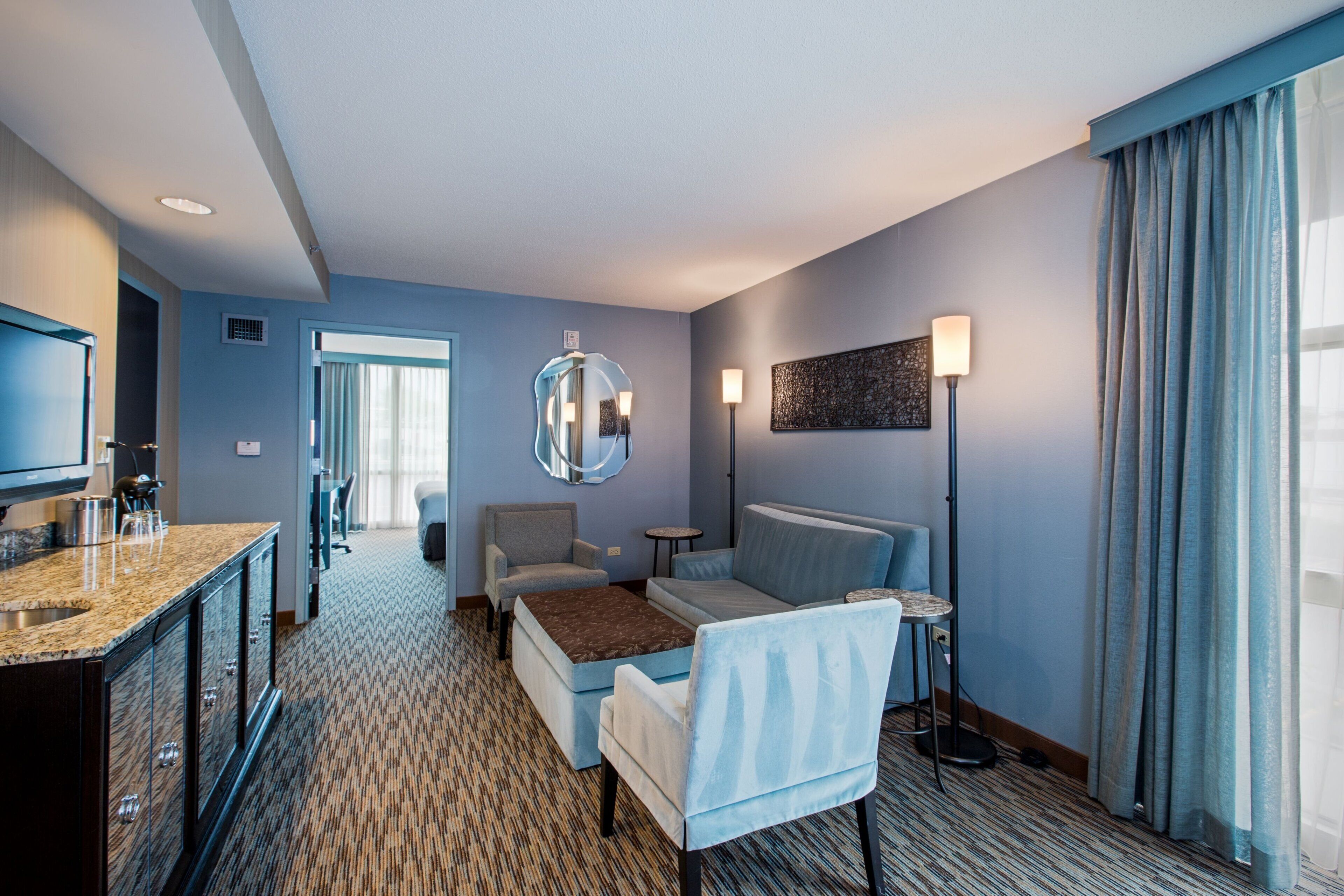 Ein Hotelzimmer mit Bett, Schreibtisch, Stuhl, Spiegel, Lampe und Fernseher.