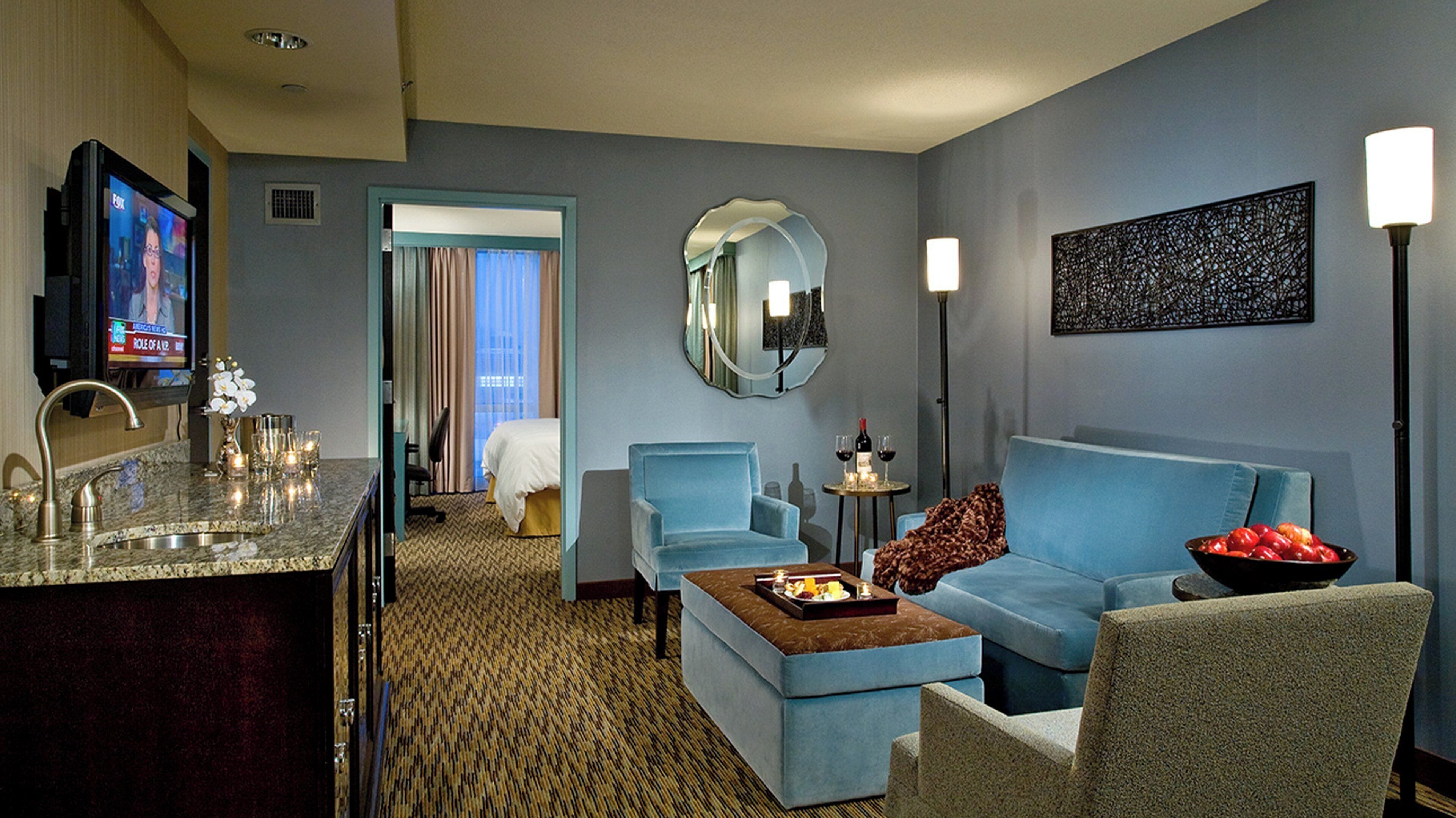 A hotel room with a living area, a dining area, a mirror, a television, and a bed.