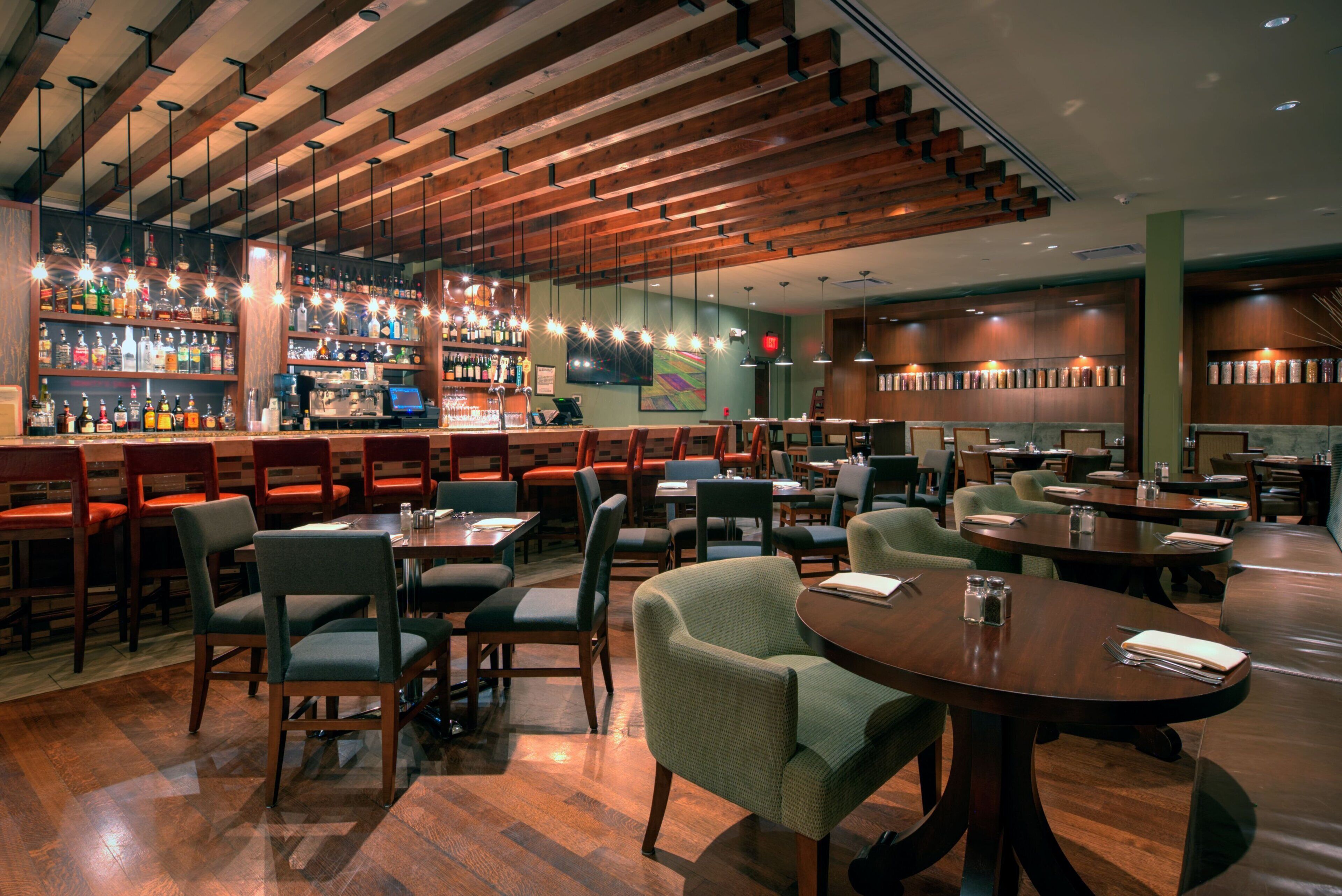 A restaurant with wooden ceiling beams, bar area with bottles, and seating arrangements.