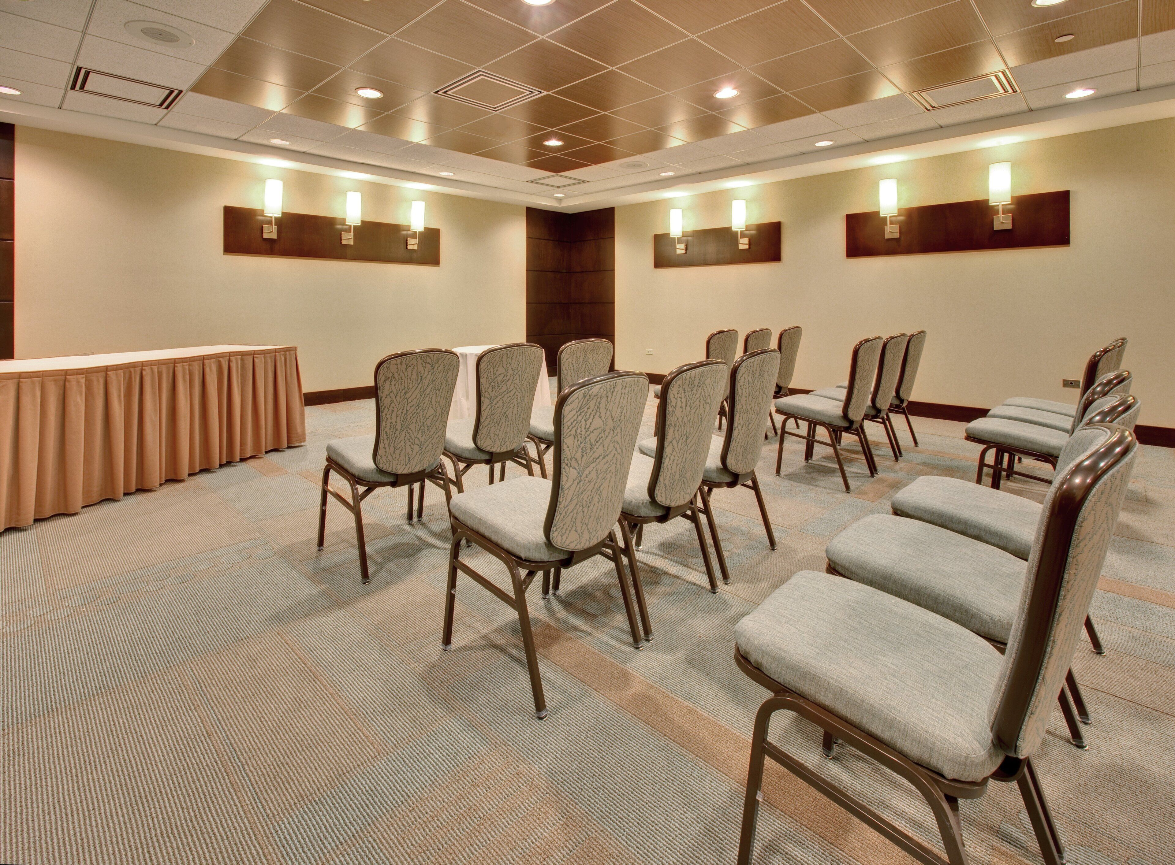 A conference room with rows of chairs, a long table, and wall-mounted lighting.
