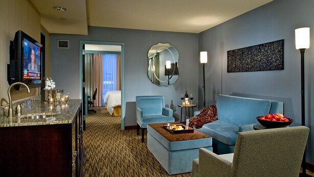 A hotel room with a living area, a dining area, a large mirror, and a television displaying a news program.