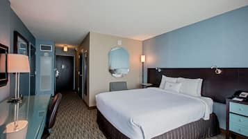 Una habitación de hotel con una cama grande, un escritorio, una silla, un espejo y una mesita de noche.