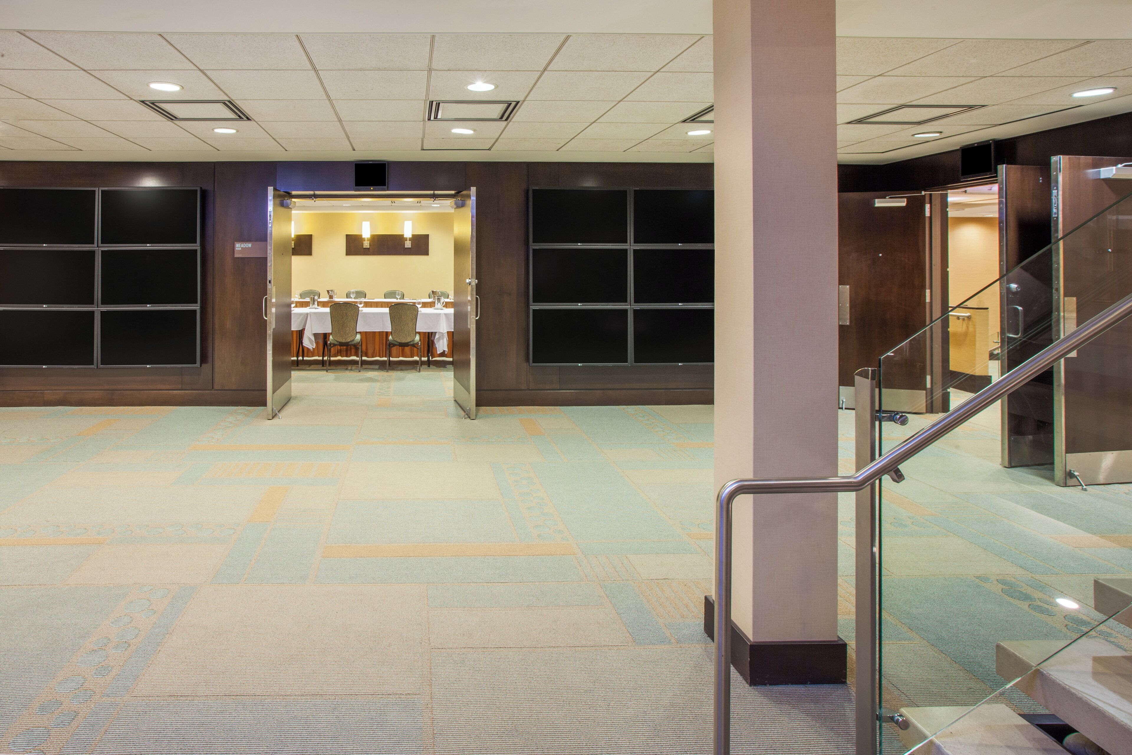 A hotel lobby with a carpeted floor, a reception desk, and a staircase.