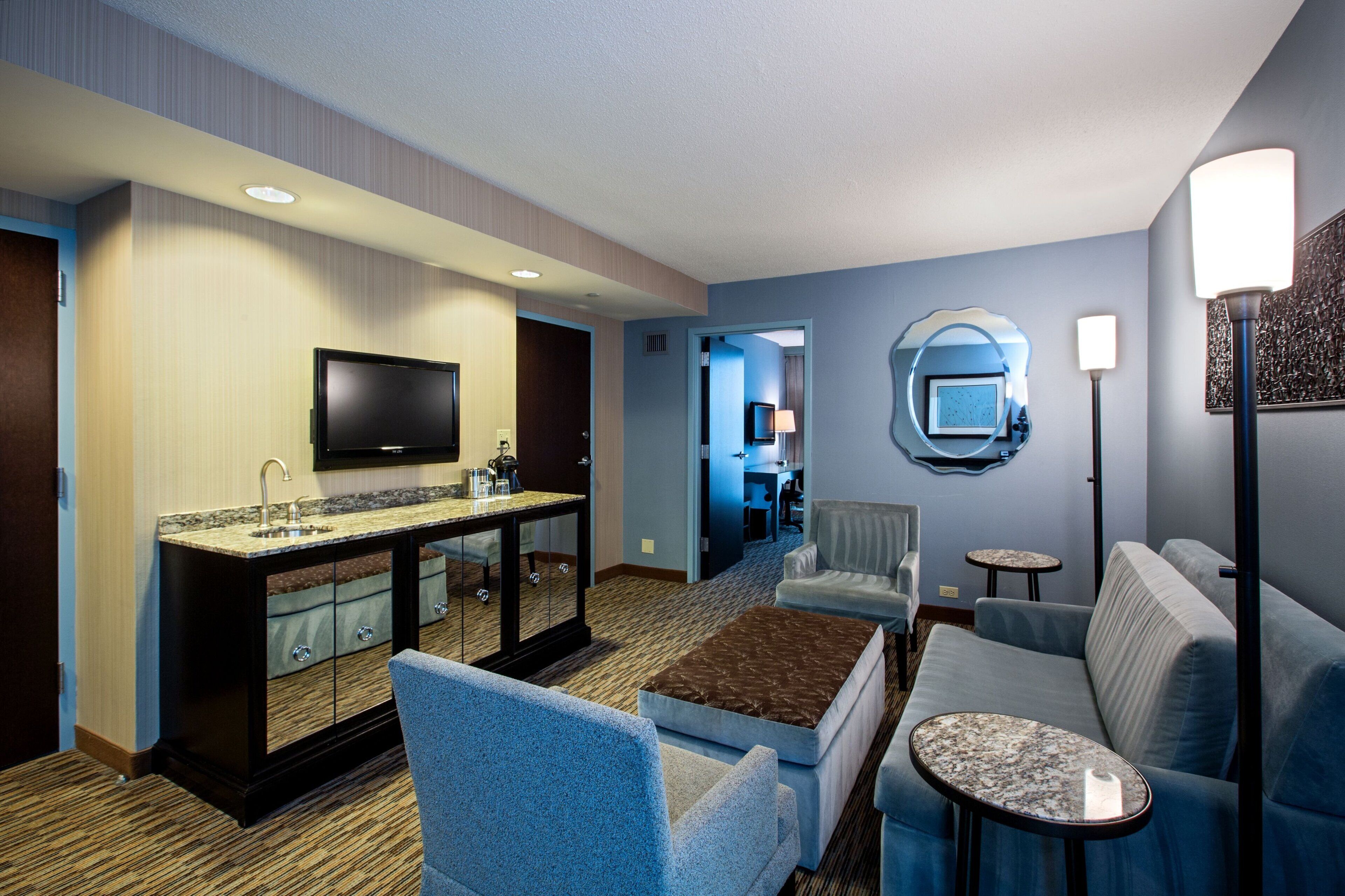 Habitación de hotel con kitchenette, televisor de pantalla plana, sofá, mesa de centro y zona de comedor.