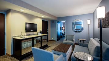 Habitación de hotel con kitchenette, televisor de pantalla plana, sofá, mesa de centro y zona de comedor.