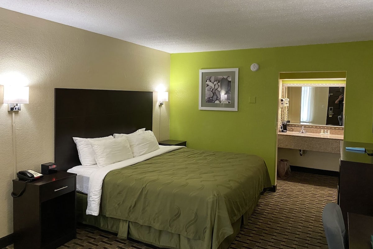 A hotel room with a bed, bedside table, lamp, and a mirror in the bathroom.