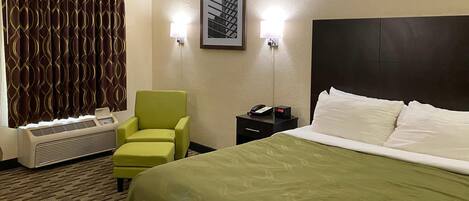 Une chambre d’hôtel avec un lit vert, un fauteuil vert, un radiateur, une table de chevet avec un téléphone et un tableau encadré au mur.