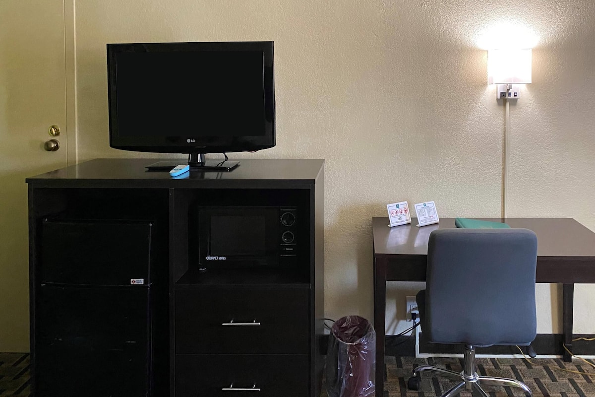 A hotel room with a minibar, a desk with a chair, a flat-screen TV, and a wall-mounted lamp.