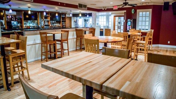 Un restaurante con mesas y sillas de madera, una zona de bar y ventiladores de techo.
