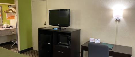 Una habitación de hotel con una cama, un escritorio con computadora, televisión y un bote de basura.