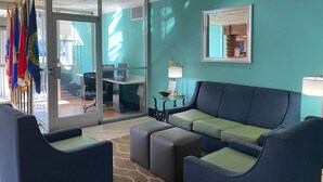Un vestíbulo moderno con una pared color turquesa, un sofá azul y una puerta de vidrio que da a un área de oficinas.