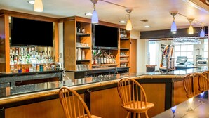 Una zona de bar con sillas de madera, una barra con botellas y una pantalla de televisión.