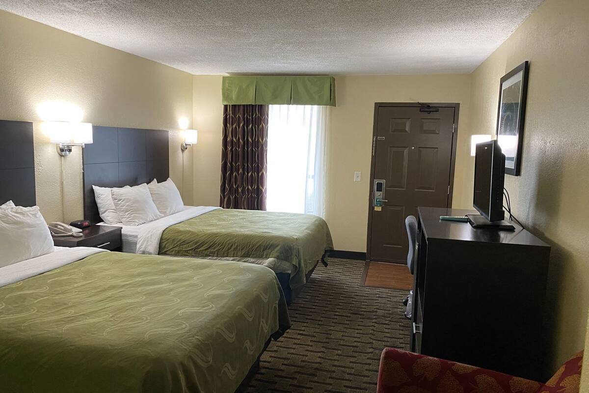 A hotel room with two beds, a desk with a computer, a phone, and a door.