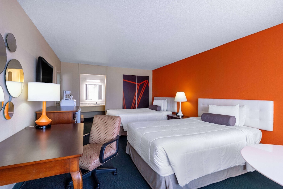 A hotel room with two beds, a desk, a chair, and a small table.