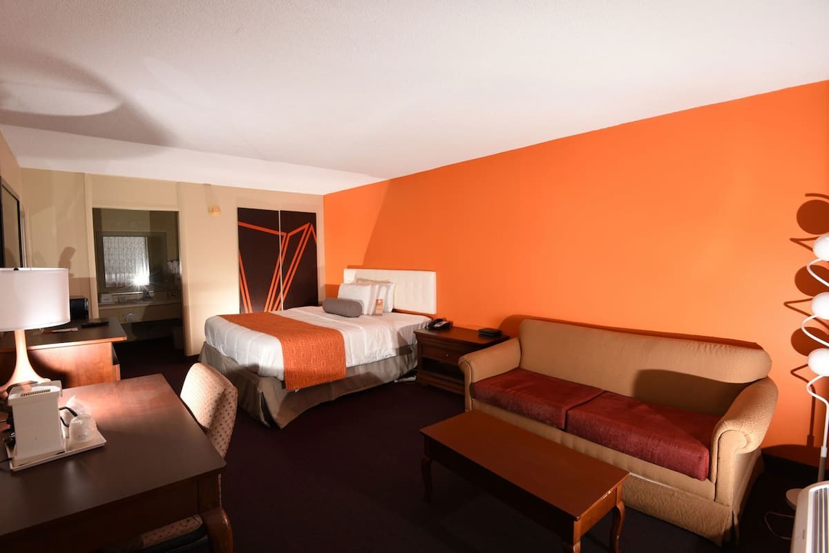A hotel room with a bed, a sofa, a desk, and a mirror.