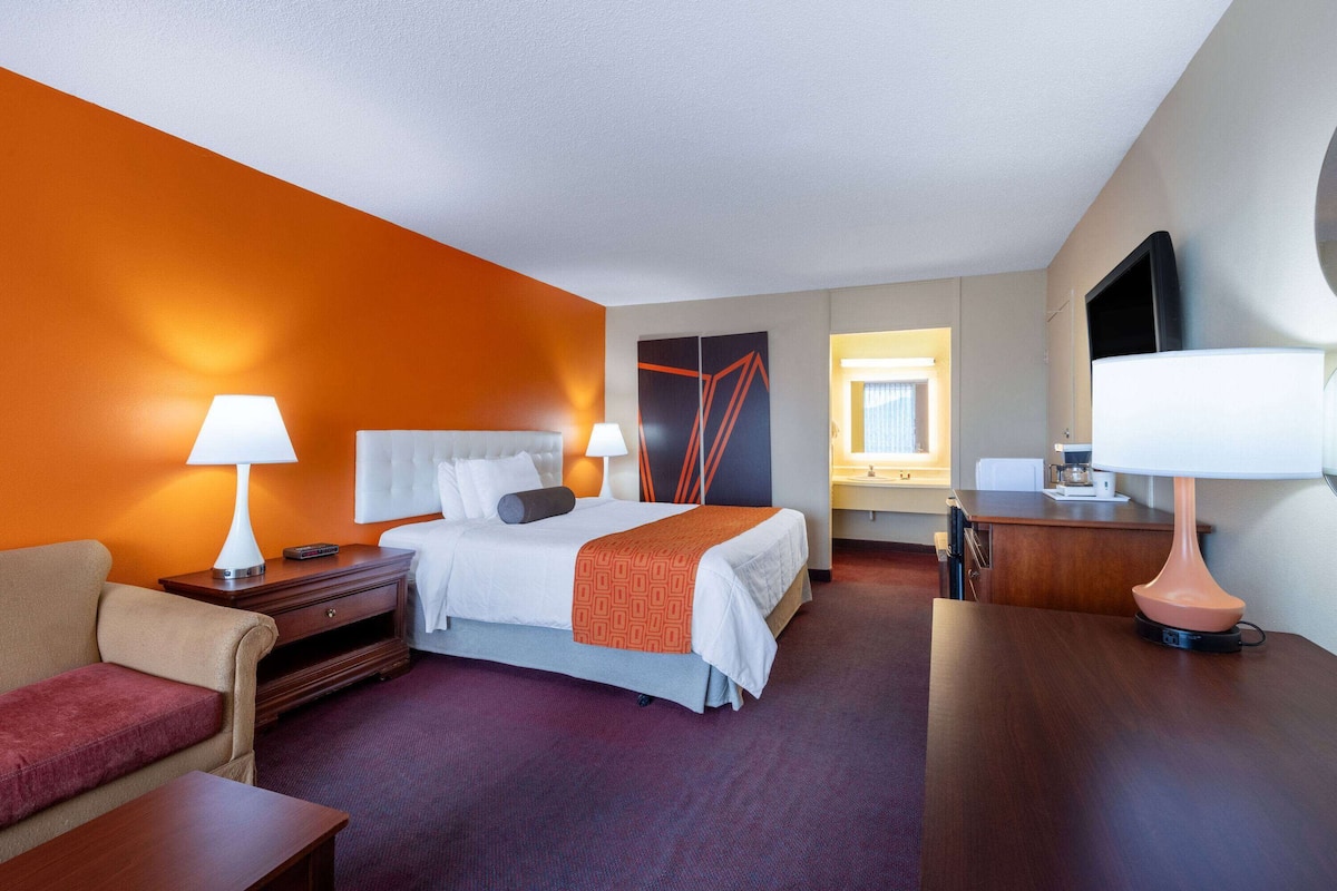 A hotel room with a bed, a desk, a chair, a sofa, and a TV.