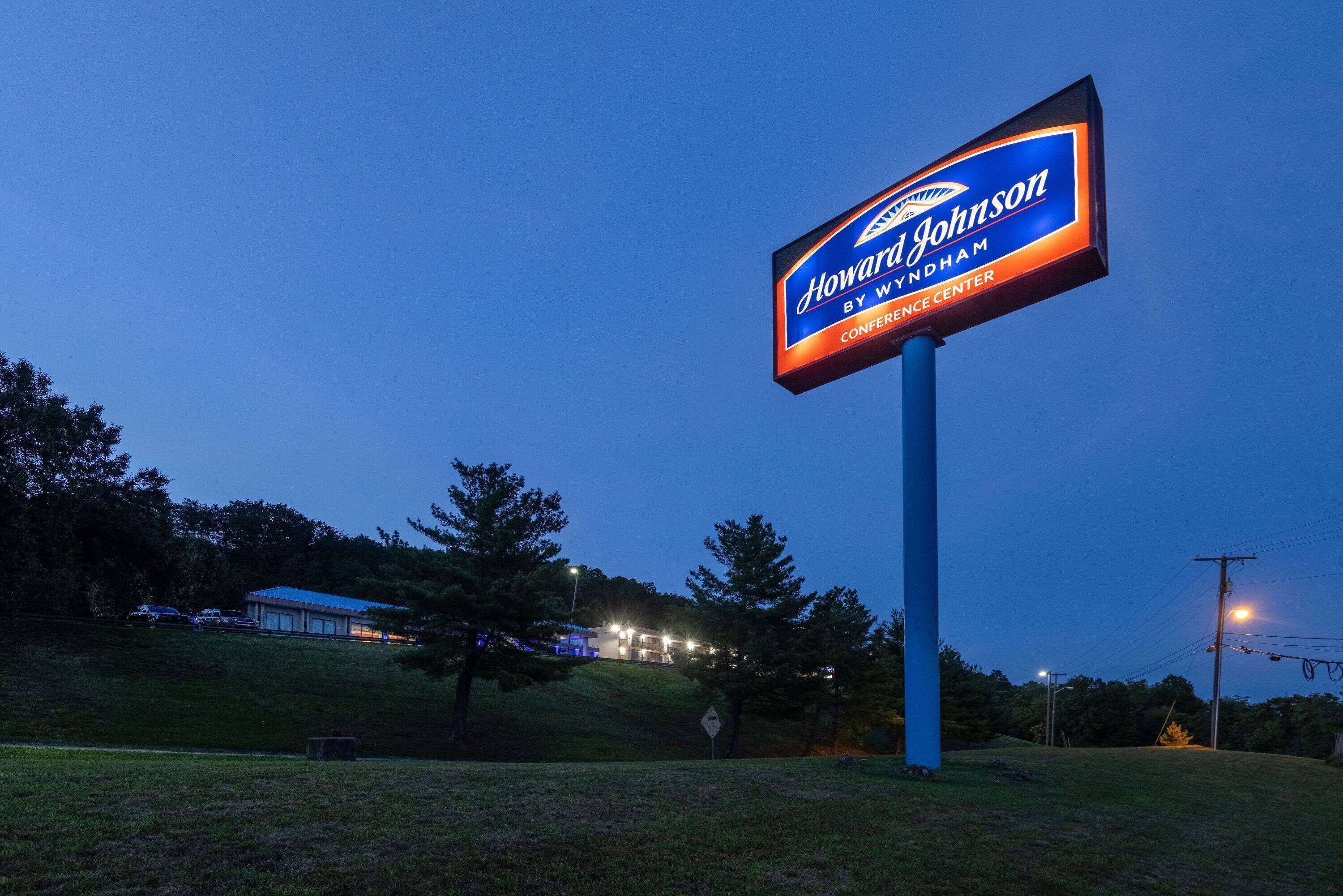 A large illuminated sign for Howard Johnson by Wyndham Conference Center against a twilight sky.