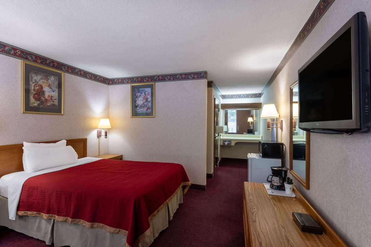 A hotel room with a bed, a desk with a coffee maker, a TV, and a mirror.
