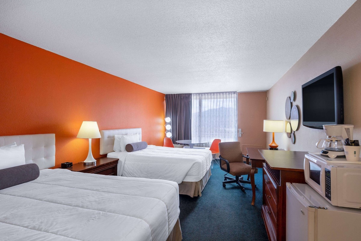 A hotel room with two beds, a desk with a computer, a television, and a coffee maker.