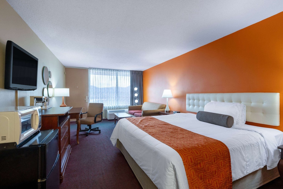 A hotel room with a large bed, a desk with a computer, a television, and a window with curtains.