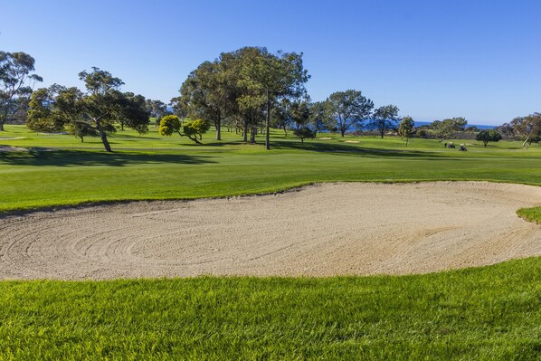 Un campo de golf con un búnker de arena, césped verde y árboles.