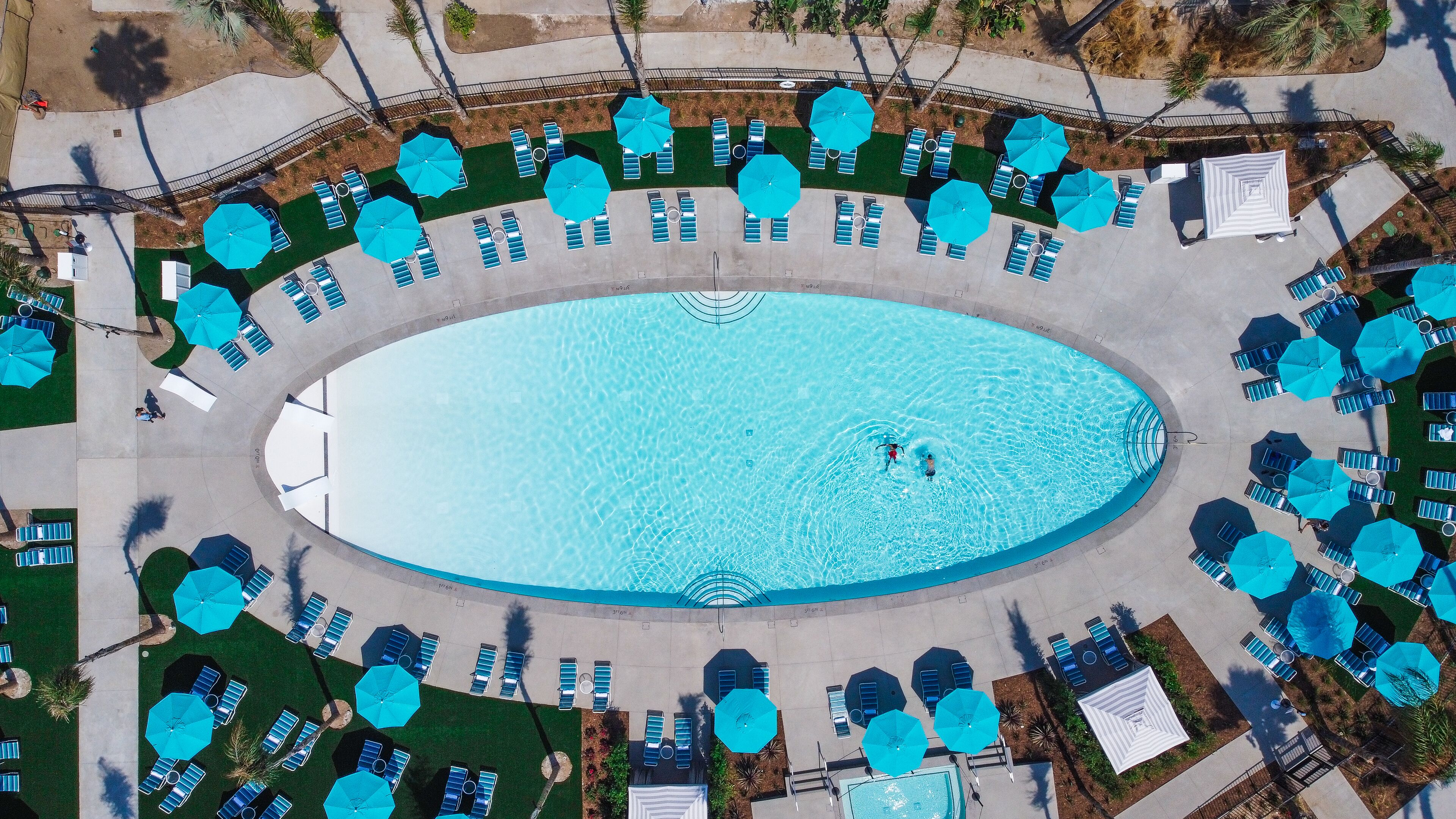 Una piscina ovalada rodeada de sillas de descanso y sombrillas, con agua cristalina.