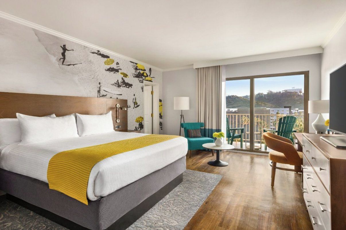 A hotel room with a large bed, a balcony with a view, a desk, and a chair.