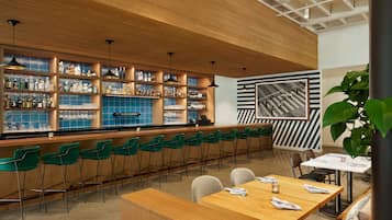 A bar area with wooden shelves, green chairs, and a seating area with tables and chairs.