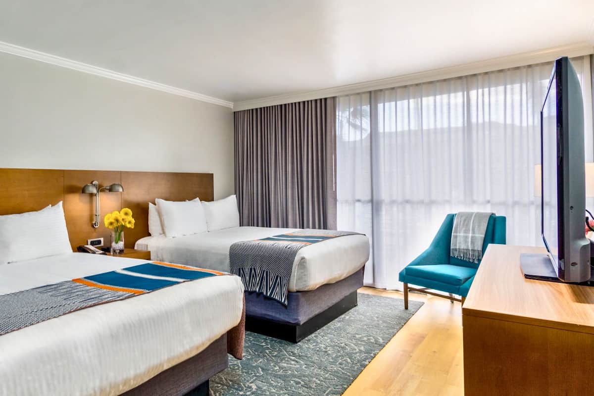 A hotel room with two beds, a desk, a chair, and a TV.