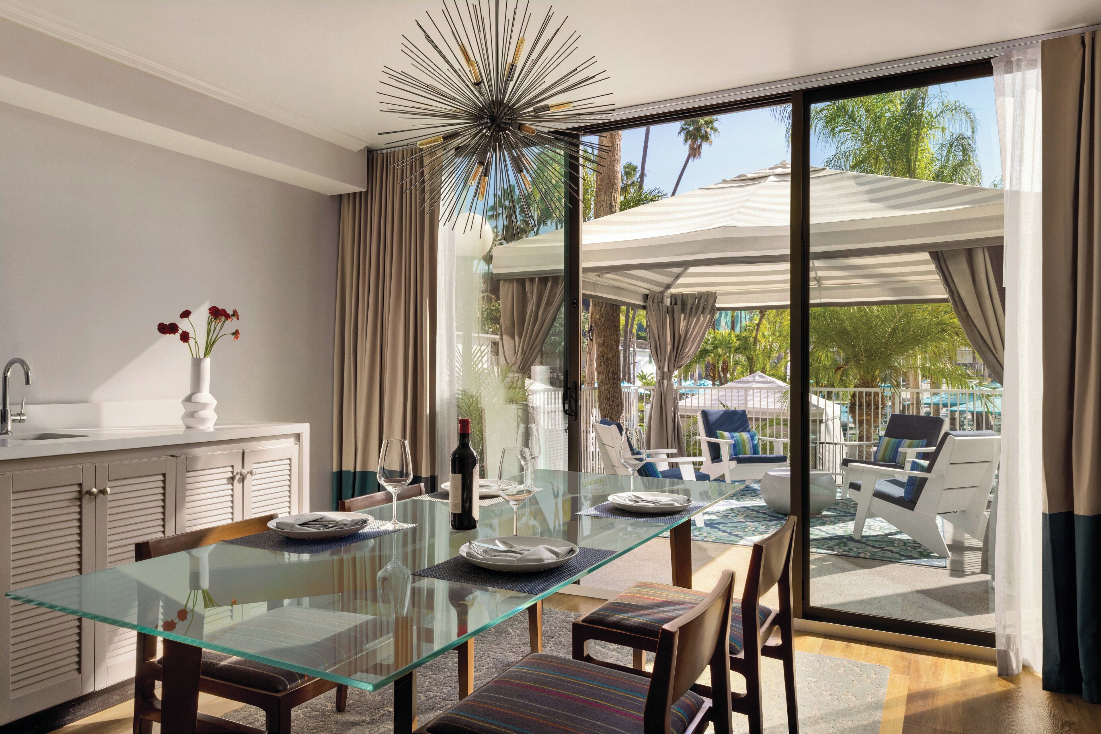 A modern dining area with a glass table, chairs, and a view of an outdoor pool and lounge chairs.