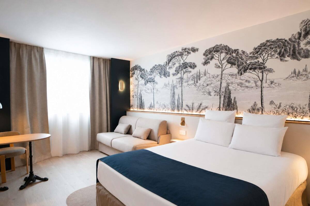 A hotel room with a bed, a desk, a chair, and a large wall mural.