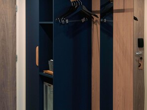 A room with a wooden door, a blue wall, a hanging coat rack, and a small shelf with items.