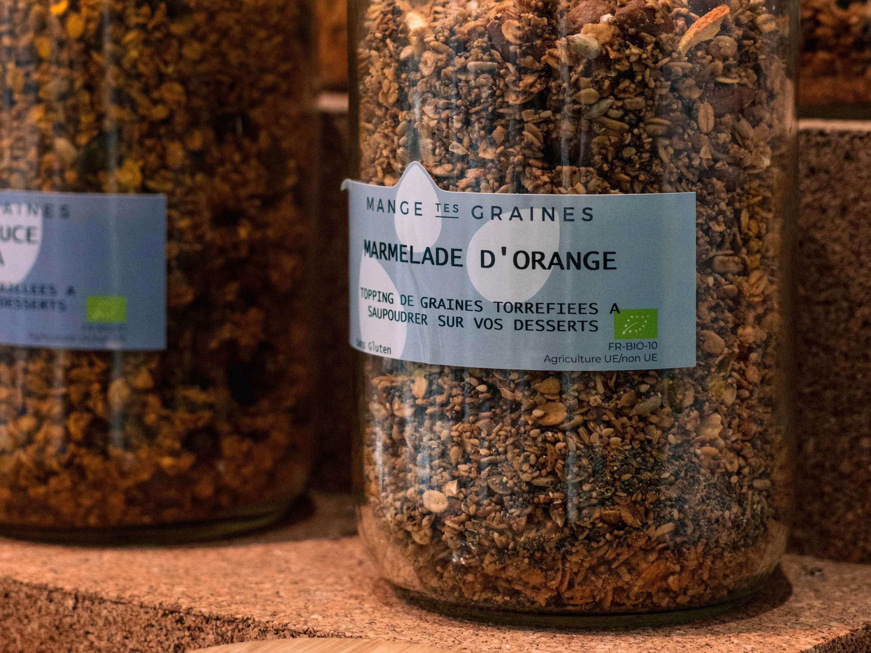 A jar of Mangle des Graines Marmalade d'Orange with a label indicating it is gluten-free and suitable for topping desserts.
