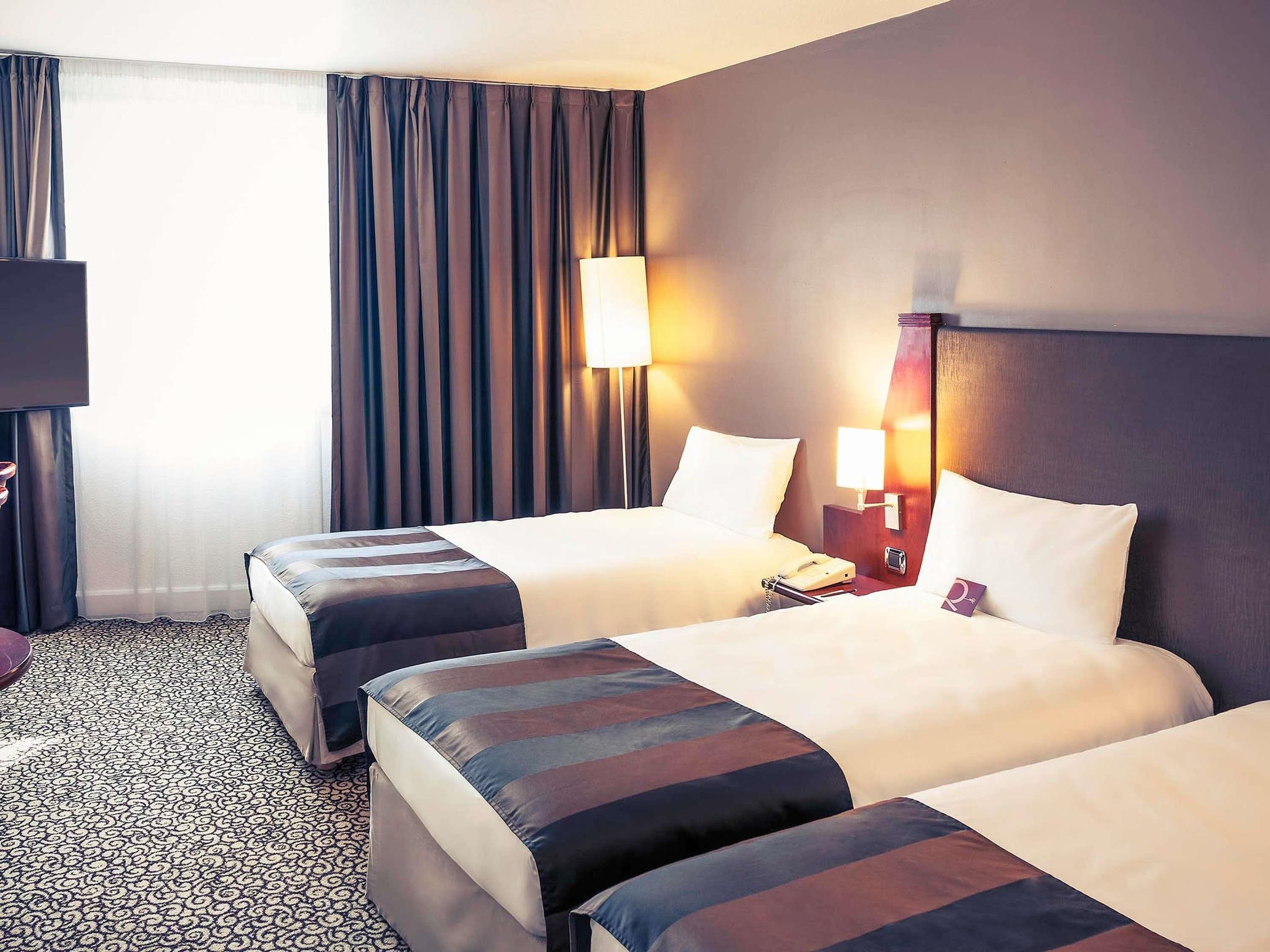 A hotel room with two beds, a desk, a lamp, and a telephone.