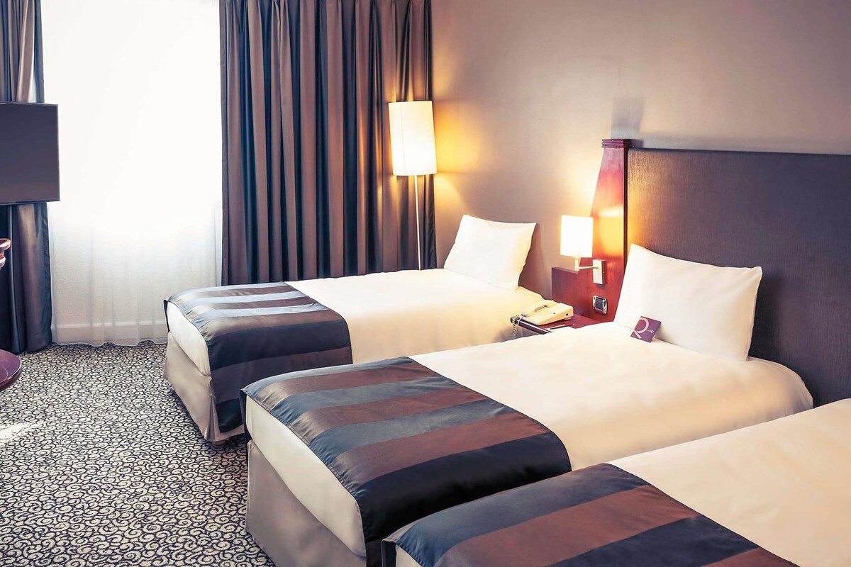 A hotel room with two beds, a desk, a lamp, and a telephone.