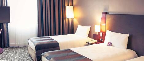 A hotel room with two beds, a desk, a lamp, and a telephone.